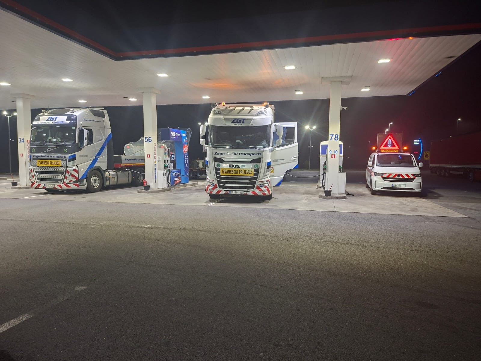 Dva tegljača Zagrebačkih transporta i prateće vozilo na benzinskoj postaji tijekom noći.